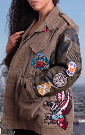 Load image into Gallery viewer, Female models side view of CdJ Hides jacket in solid khaki vest with camo leather sleeves and patch embellishments.
