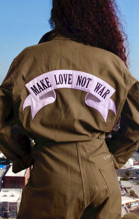 Load image into Gallery viewer, Female models back view of CdJ Olive Drab jumper with &quot;Make Love Not War&quot; patch emblazoned on the back.
